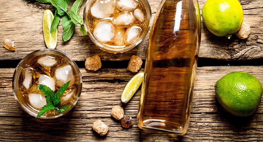 Cocktails with lime, ice and a bottle of rum on a wooden table